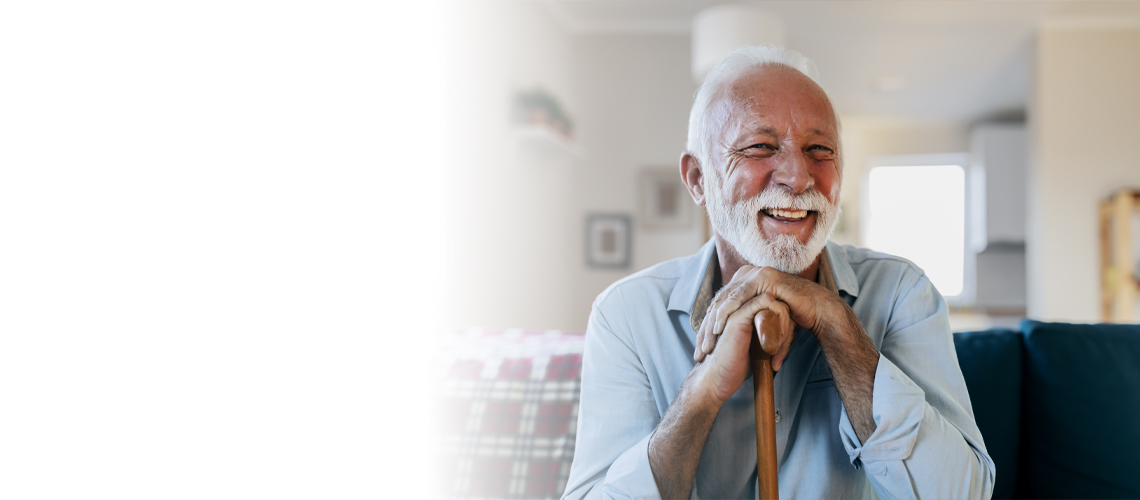 Portrait of happy senior man sitting in living room with walking cane