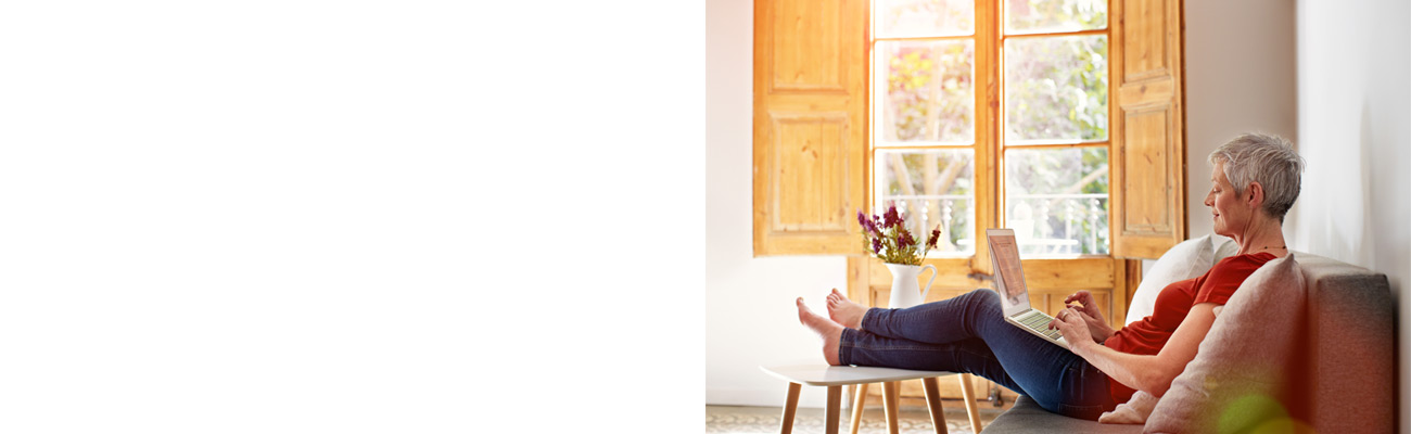 Older woman sitting on couch scrolling on laptop
