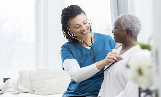Nurse placing stethoscope on older patient