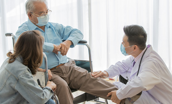 Older man sitting in wheelchair while doctor exams leg